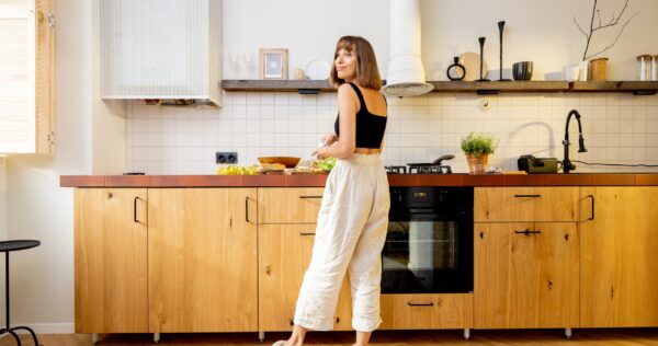 Mujer sonriendo y cocinando, al ver que su cocina está ordenada y recogida gracias al servicio de limpieza profesional de Mamaju.